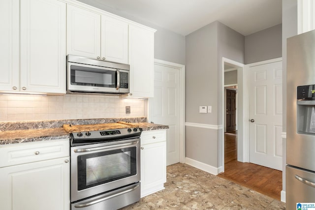 kitchen with appliances with stainless steel finishes, backsplash, light hardwood / wood-style flooring, dark stone countertops, and white cabinets