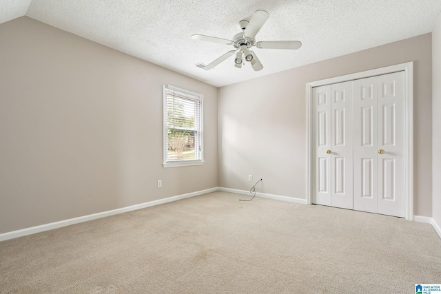 unfurnished bedroom with ceiling fan, a textured ceiling, vaulted ceiling, light carpet, and a closet