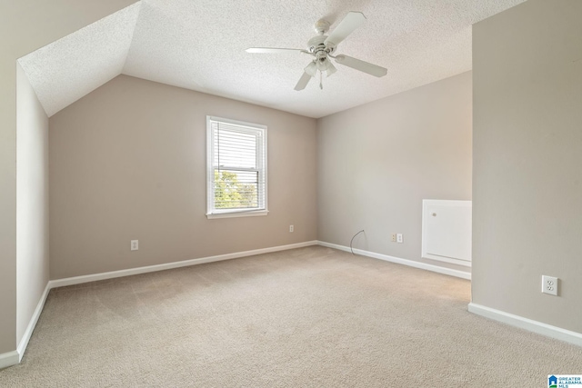 empty room featuring a textured ceiling, light colored carpet, ceiling fan, and lofted ceiling