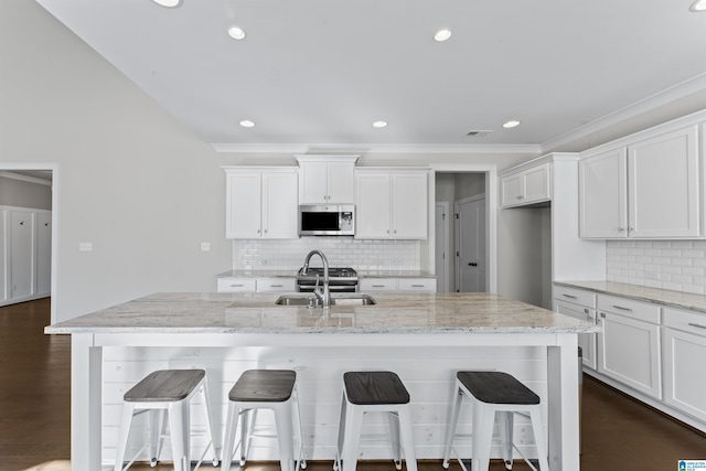 kitchen featuring decorative backsplash, light stone counters, sink, white cabinets, and an island with sink