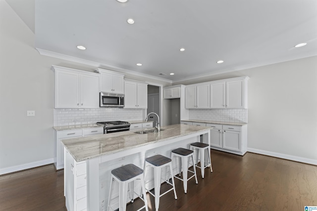 kitchen featuring white cabinetry, stainless steel appliances, dark hardwood / wood-style floors, a center island with sink, and ornamental molding