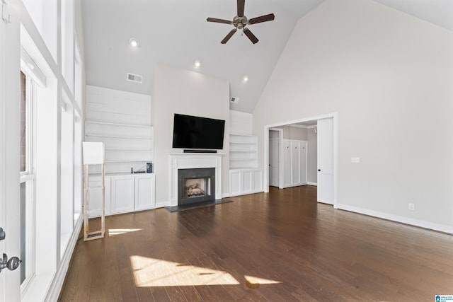 unfurnished living room with built in shelves, ceiling fan, high vaulted ceiling, and dark wood-type flooring