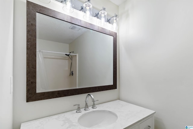 bathroom with a textured ceiling, vanity, and walk in shower