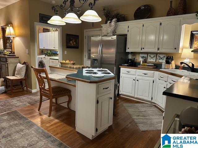 kitchen with white cabinetry, sink, hanging light fixtures, washer / dryer, and a kitchen island