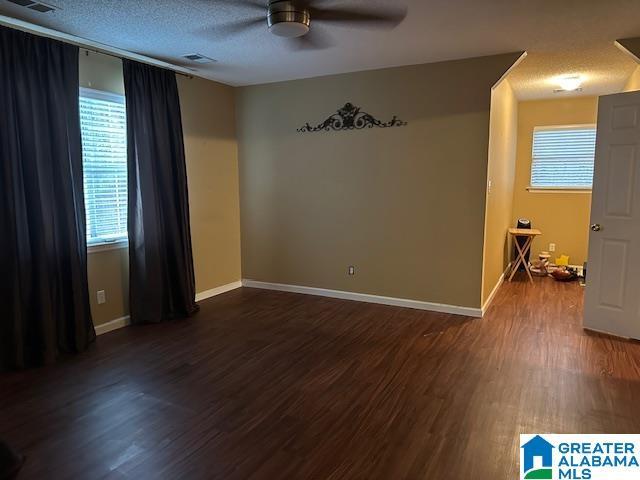 empty room with ceiling fan, dark wood-type flooring, and a textured ceiling