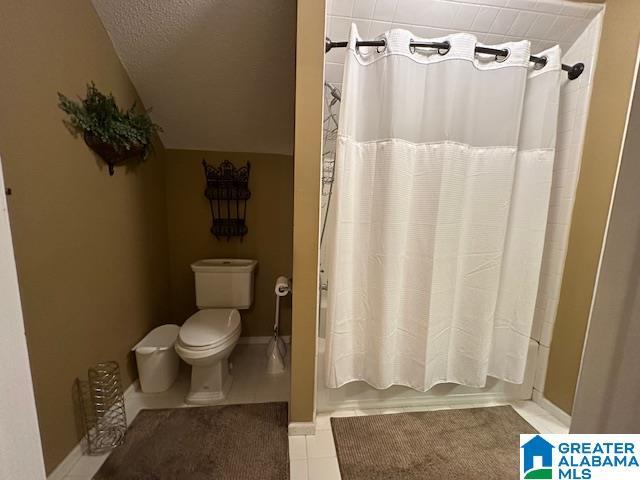 bathroom with tile patterned flooring, vaulted ceiling, shower / tub combo with curtain, and toilet