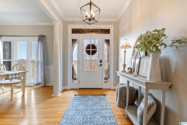 entryway featuring light wood-type flooring, an inviting chandelier, crown molding, and ornate columns