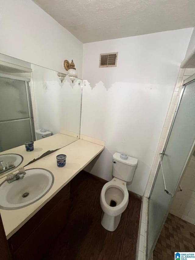 bathroom with a textured ceiling, vanity, a shower with door, hardwood / wood-style flooring, and toilet