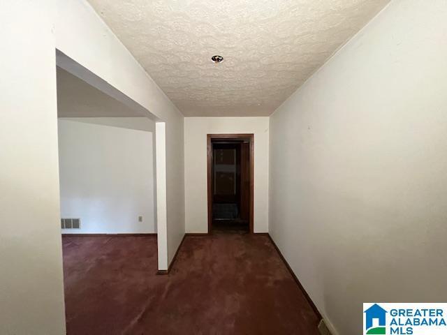 hallway with dark carpet and a textured ceiling