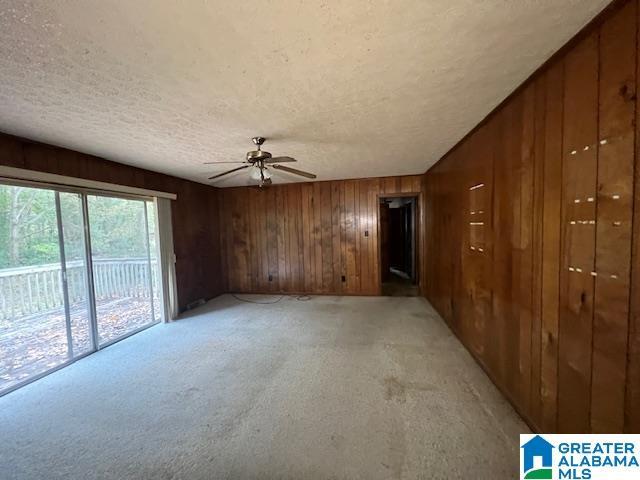 empty room with ceiling fan, wooden walls, light colored carpet, and a textured ceiling