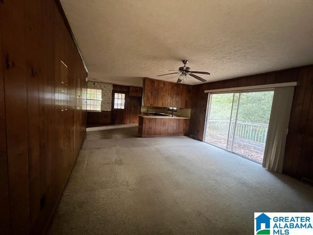 unfurnished living room with ceiling fan, light colored carpet, a textured ceiling, and wooden walls