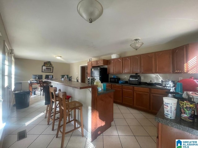 kitchen with a kitchen bar, a kitchen island, black appliances, and light tile patterned floors