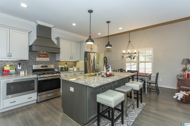 kitchen with premium range hood, an island with sink, decorative light fixtures, a breakfast bar, and appliances with stainless steel finishes