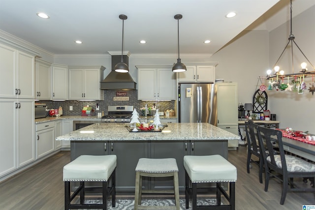 kitchen featuring light stone countertops, custom exhaust hood, stainless steel appliances, decorative light fixtures, and a kitchen island