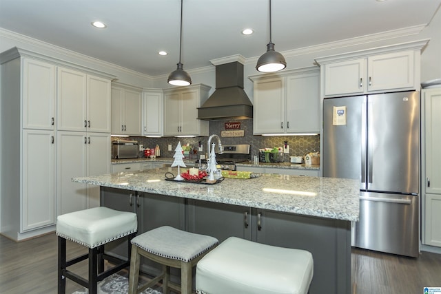 kitchen with premium range hood, dark hardwood / wood-style floors, an island with sink, appliances with stainless steel finishes, and light stone counters