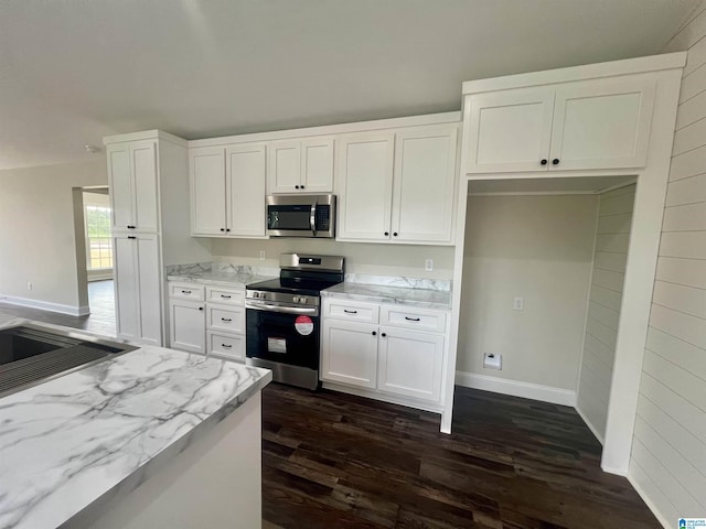 kitchen with appliances with stainless steel finishes, dark hardwood / wood-style flooring, light stone counters, sink, and white cabinets