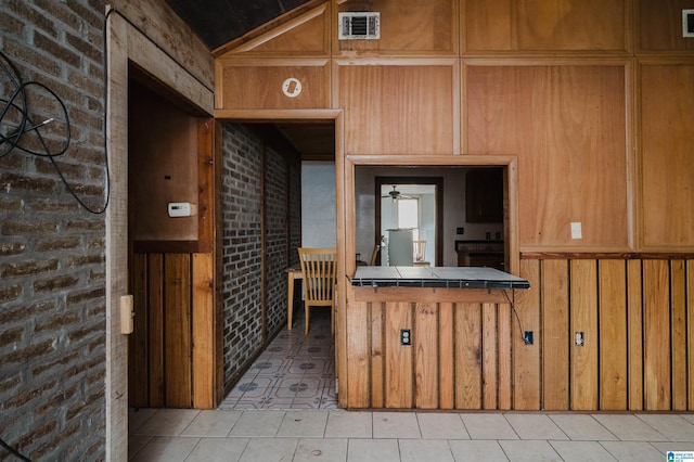 interior space with wooden walls, tile counters, ceiling fan, and brick wall