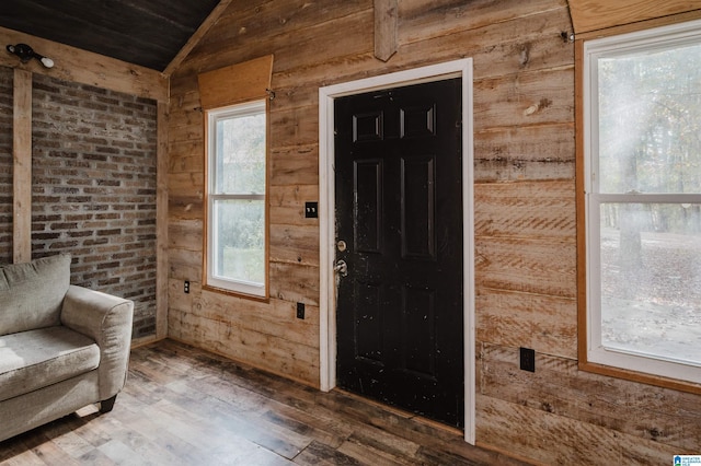 foyer with hardwood / wood-style floors, wooden walls, lofted ceiling, and brick wall