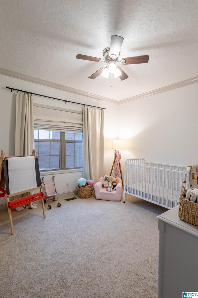 unfurnished bedroom with ceiling fan, ornamental molding, a textured ceiling, a nursery area, and carpet floors