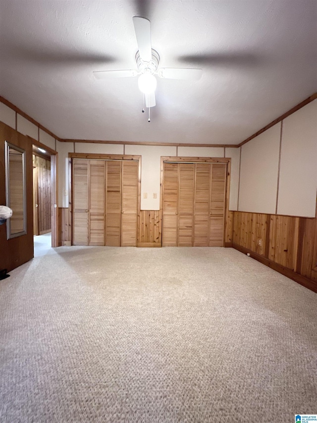 interior space with light carpet, ornamental molding, a textured ceiling, ceiling fan, and wood walls