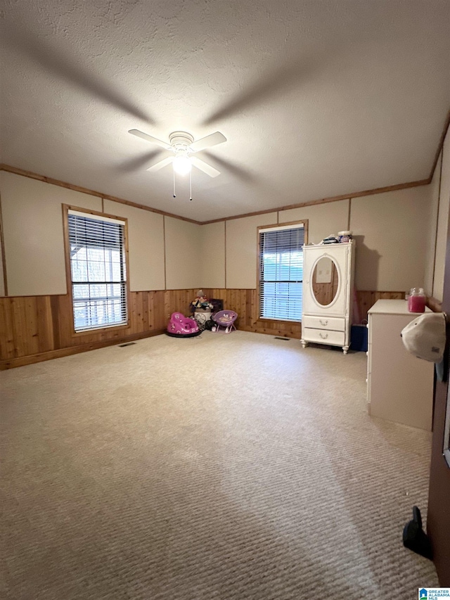 unfurnished room with wooden walls, carpet flooring, ceiling fan, ornamental molding, and a textured ceiling