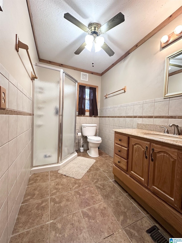 bathroom with vanity, a textured ceiling, a shower with door, crown molding, and tile walls