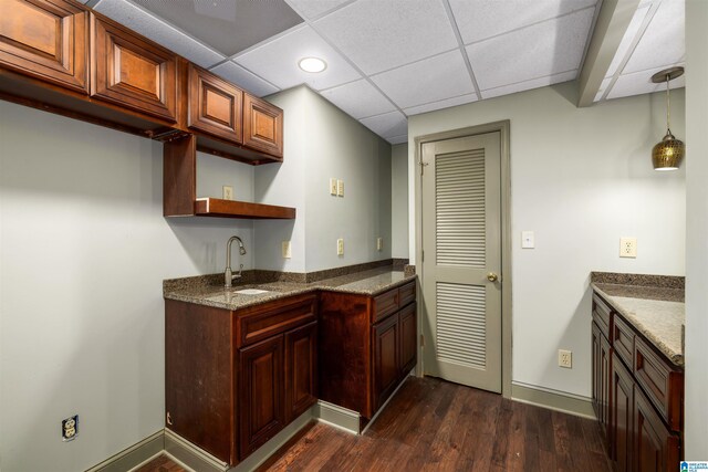 kitchen with a drop ceiling, dark wood-type flooring, dark stone counters, sink, and hanging light fixtures