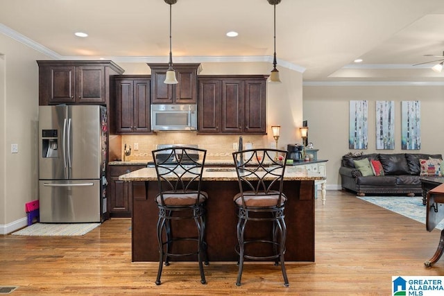 kitchen with a kitchen bar, light wood-type flooring, a kitchen island, light stone counters, and stainless steel appliances