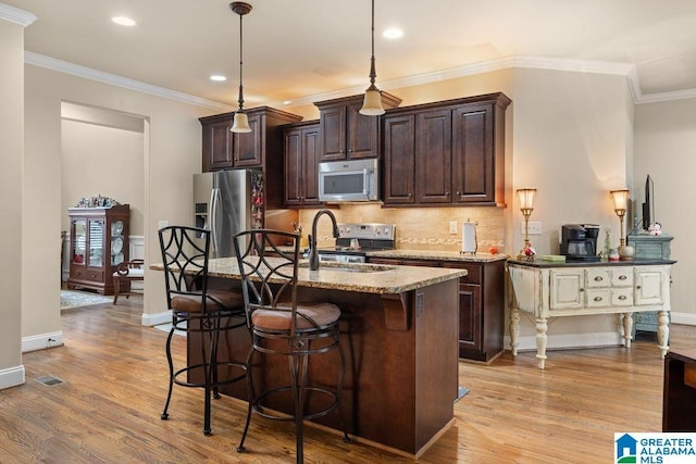 kitchen featuring decorative light fixtures, light wood-type flooring, stainless steel appliances, and a center island with sink