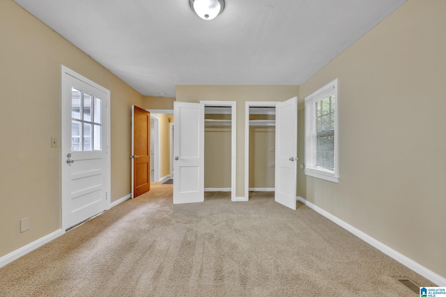 unfurnished bedroom featuring light carpet and two closets