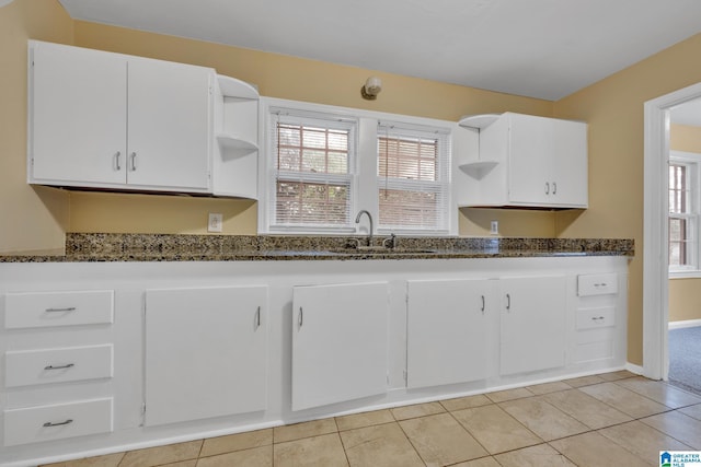 kitchen with light tile patterned floors, sink, white cabinetry, and dark stone countertops