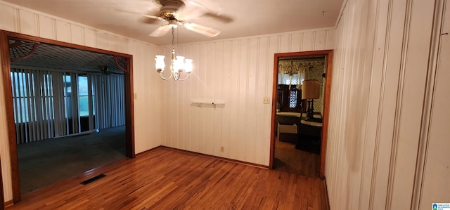 unfurnished dining area featuring crown molding, hardwood / wood-style floors, ceiling fan with notable chandelier, and wooden walls