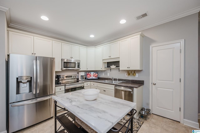 kitchen with sink, dark stone countertops, appliances with stainless steel finishes, white cabinets, and ornamental molding