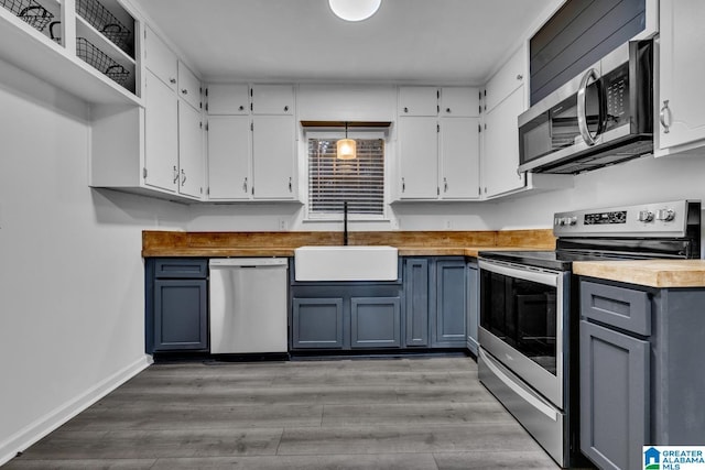 kitchen with sink, stainless steel appliances, light hardwood / wood-style flooring, butcher block countertops, and decorative light fixtures