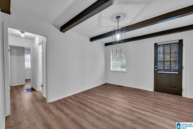 unfurnished dining area with a textured ceiling, light hardwood / wood-style floors, beam ceiling, and a wealth of natural light