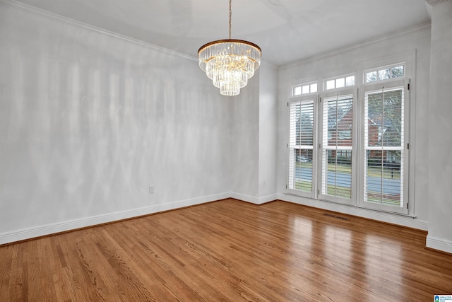 empty room with hardwood / wood-style floors, a healthy amount of sunlight, crown molding, and a chandelier