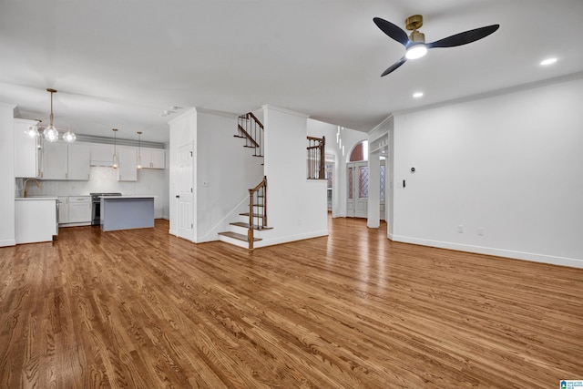 unfurnished living room with ceiling fan, light hardwood / wood-style floors, ornamental molding, and sink