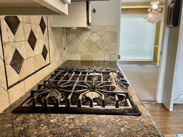 kitchen with a notable chandelier, backsplash, black gas stovetop, dark stone counters, and wood-type flooring