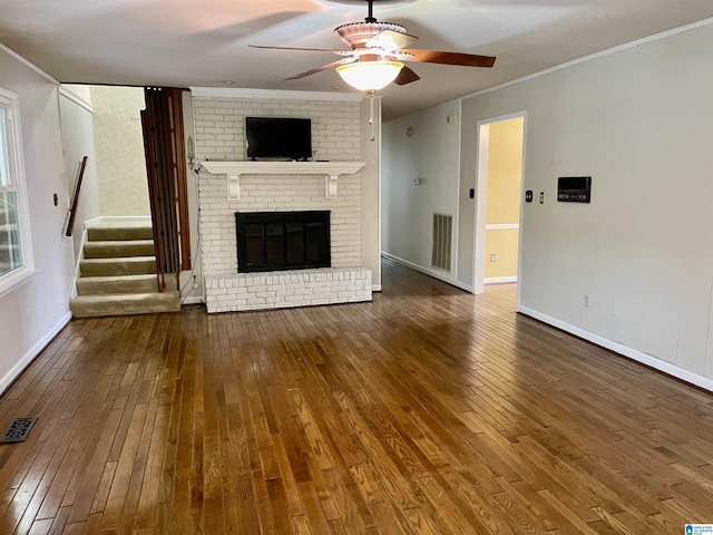 unfurnished living room with a brick fireplace, ceiling fan, crown molding, and hardwood / wood-style flooring