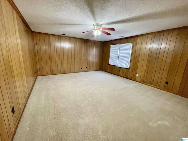 spare room with a textured ceiling, ceiling fan, light carpet, and wooden walls