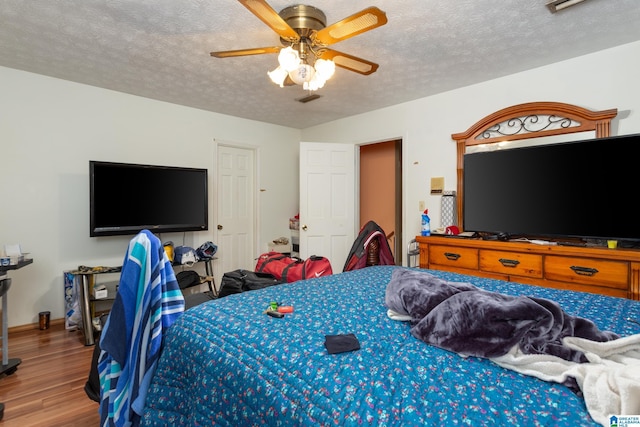 bedroom with ceiling fan, wood-type flooring, and a textured ceiling