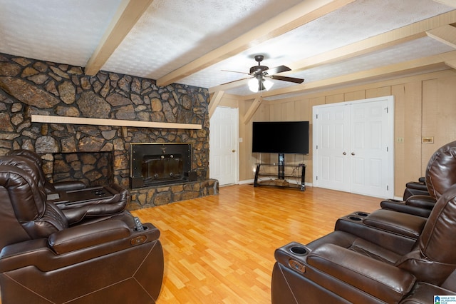 living room with a textured ceiling, ceiling fan, hardwood / wood-style flooring, beamed ceiling, and a stone fireplace