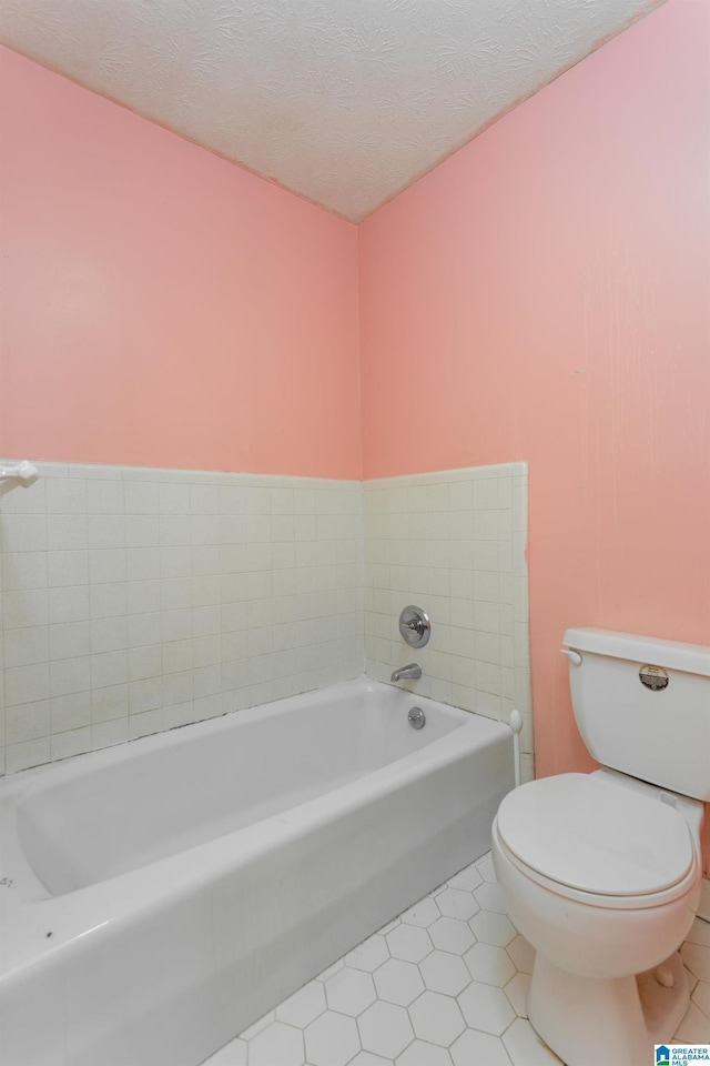 bathroom with tile patterned floors, a tub to relax in, toilet, and a textured ceiling