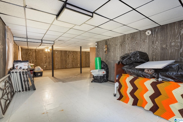 basement featuring a drop ceiling and wooden walls