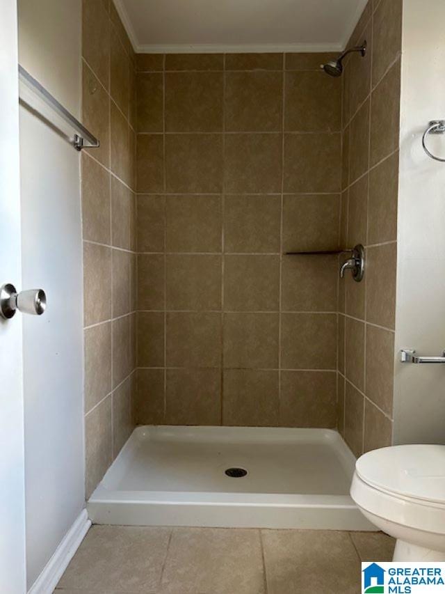 bathroom with tile patterned floors, crown molding, toilet, and tiled shower