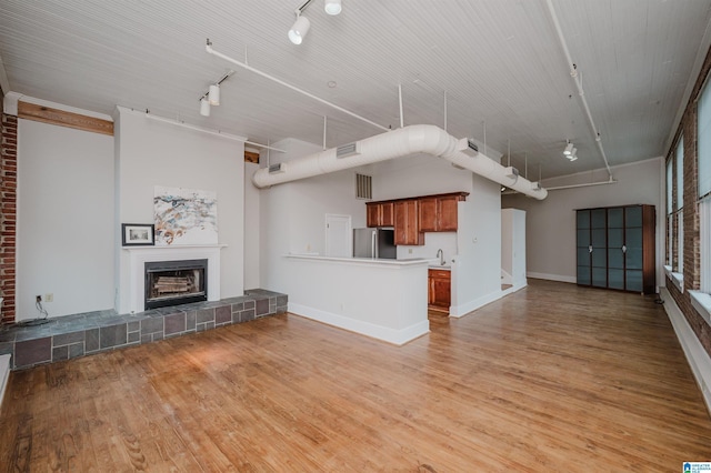 unfurnished living room featuring rail lighting, light wood-type flooring, sink, and a tiled fireplace