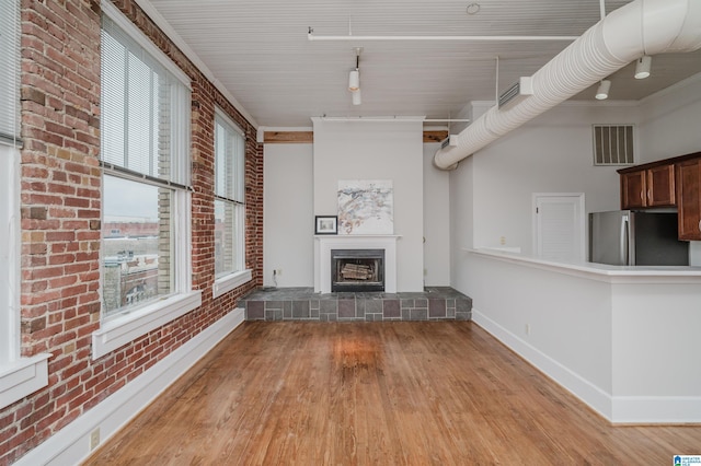 unfurnished living room with crown molding, plenty of natural light, brick wall, and light hardwood / wood-style flooring