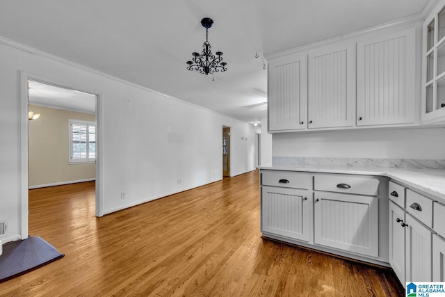 kitchen with crown molding, white cabinets, hanging light fixtures, and light wood-type flooring