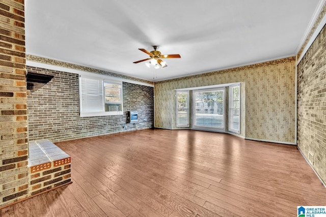 unfurnished living room featuring hardwood / wood-style floors, a healthy amount of sunlight, brick wall, and ornamental molding