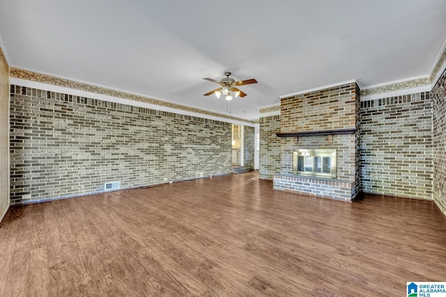 unfurnished living room featuring ceiling fan, wood-type flooring, a fireplace, and brick wall